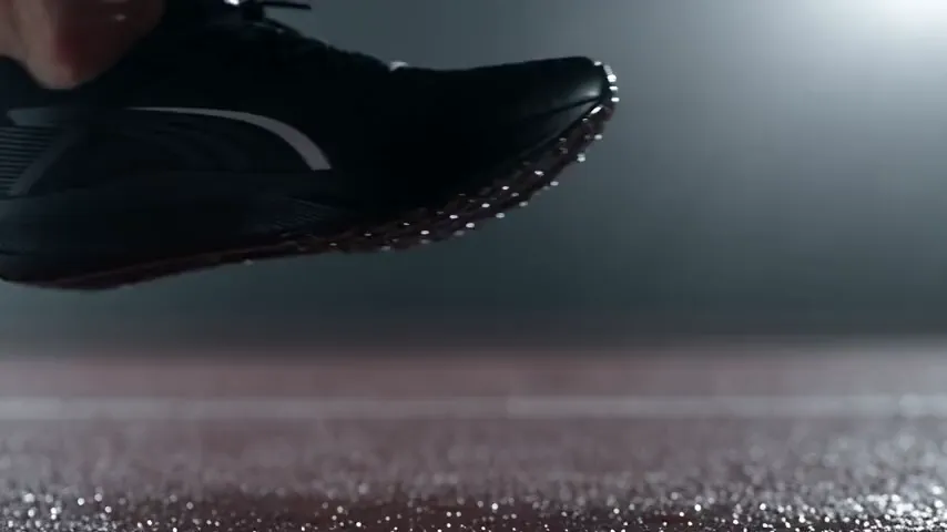 Seedance 2.5 test render of the running shoe prompt: a black running shoe comes down toward a wet track, plants on it, and pushes off as water droplets scatter.